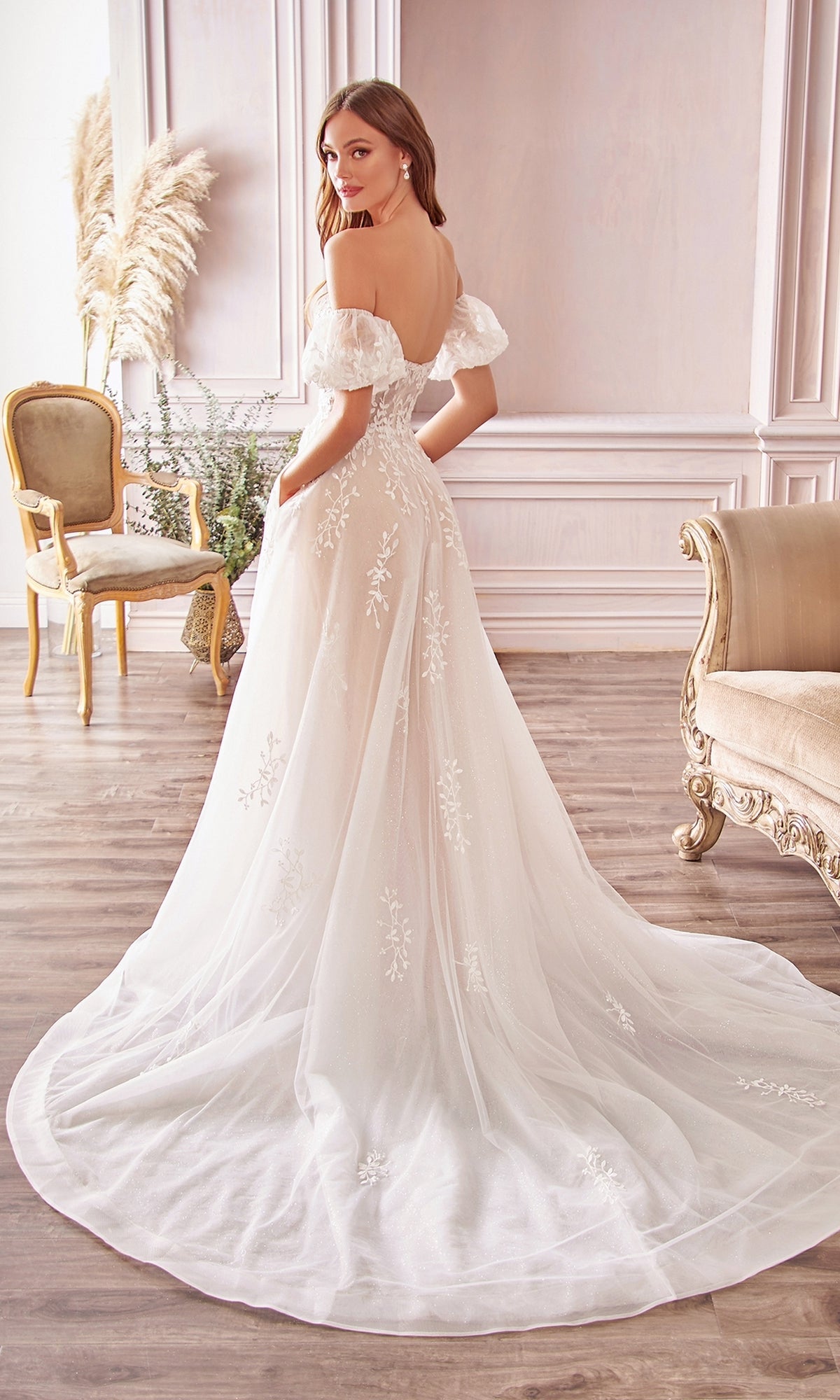 A woman stands in an elegant room wearing the Puff-Sleeve Long White Wedding Dress A1014, featuring floral lace details, removable puff sleeves, and a long train.
